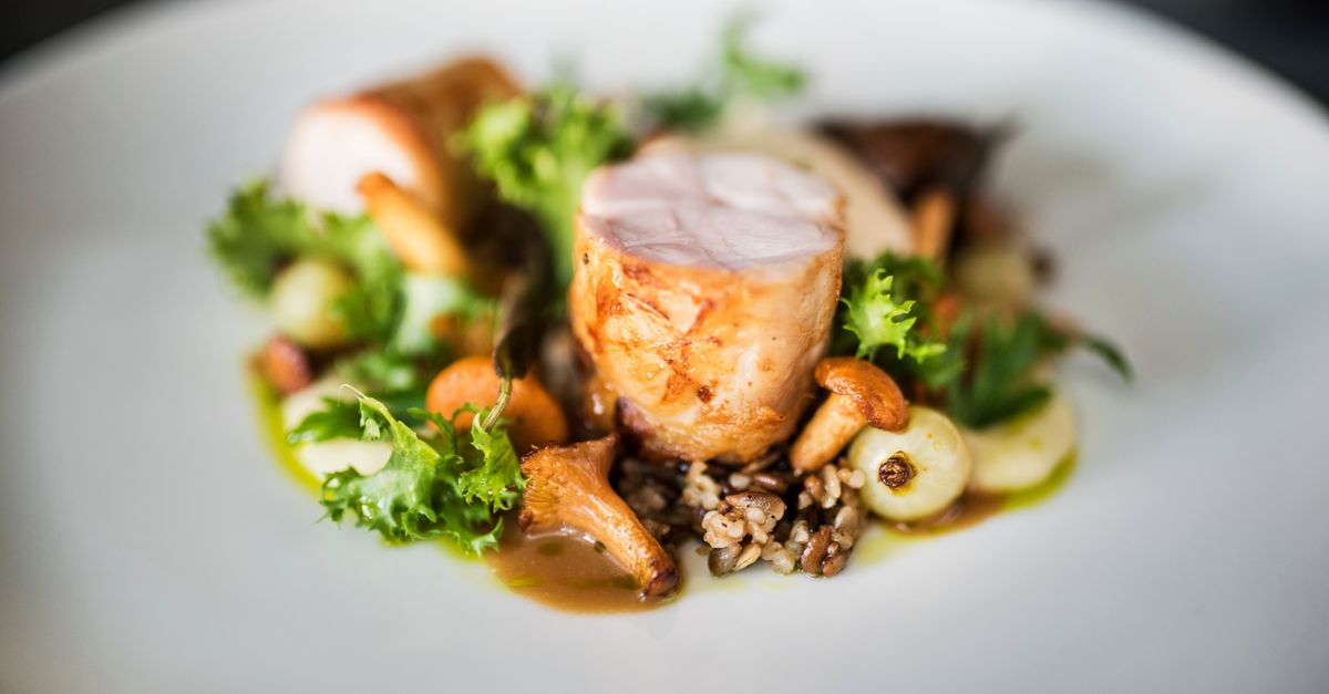 Close-up of a gourmet chicken dish with wild rice, mushrooms, and greens on a white plate.