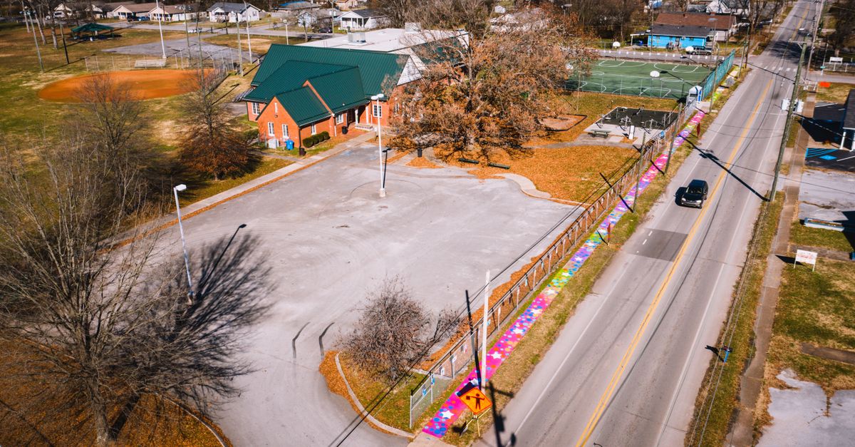 Drone view of asphalt roadway with car driving between houses and bright graffiti on wall in suburb area
