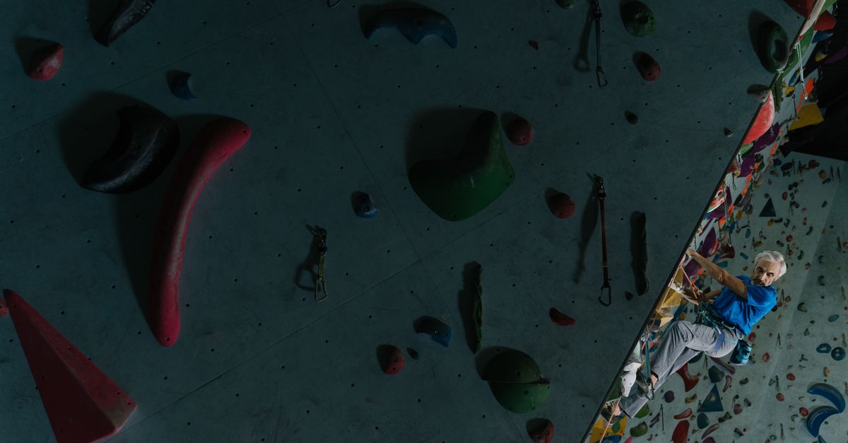A senior man skillfully climbing an indoor bouldering wall challenges age limits.