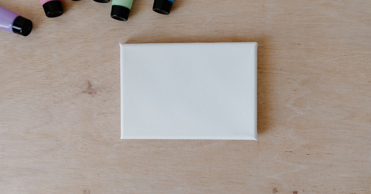 Top view of colorful paint tubes and blank canvas on a wooden surface.