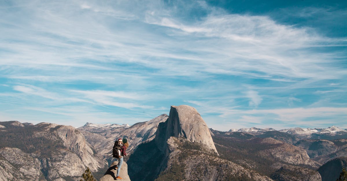 A woman and child stand atop Half Dome, Yosemite, with breathtaking views of the mountain range.