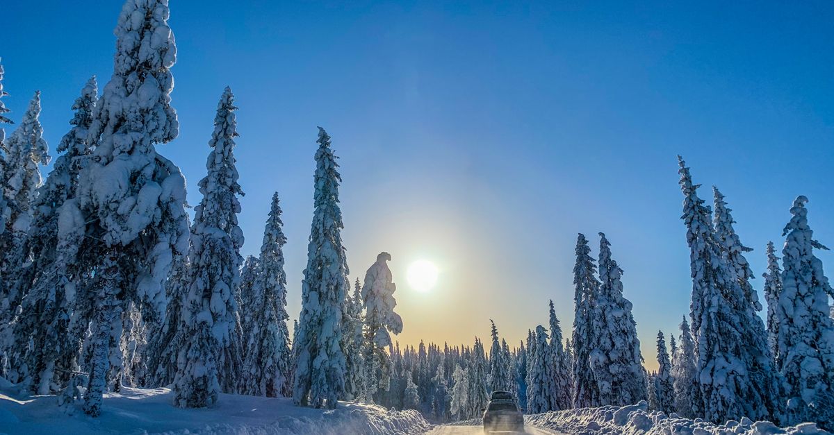 A car drives through a snowy forest under a bright sun in Torsby, Sweden, capturing a serene winter landscape.