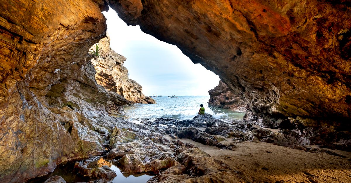 Explore the stunning view from a rocky beach cave, revealing the serene sea beyond.
