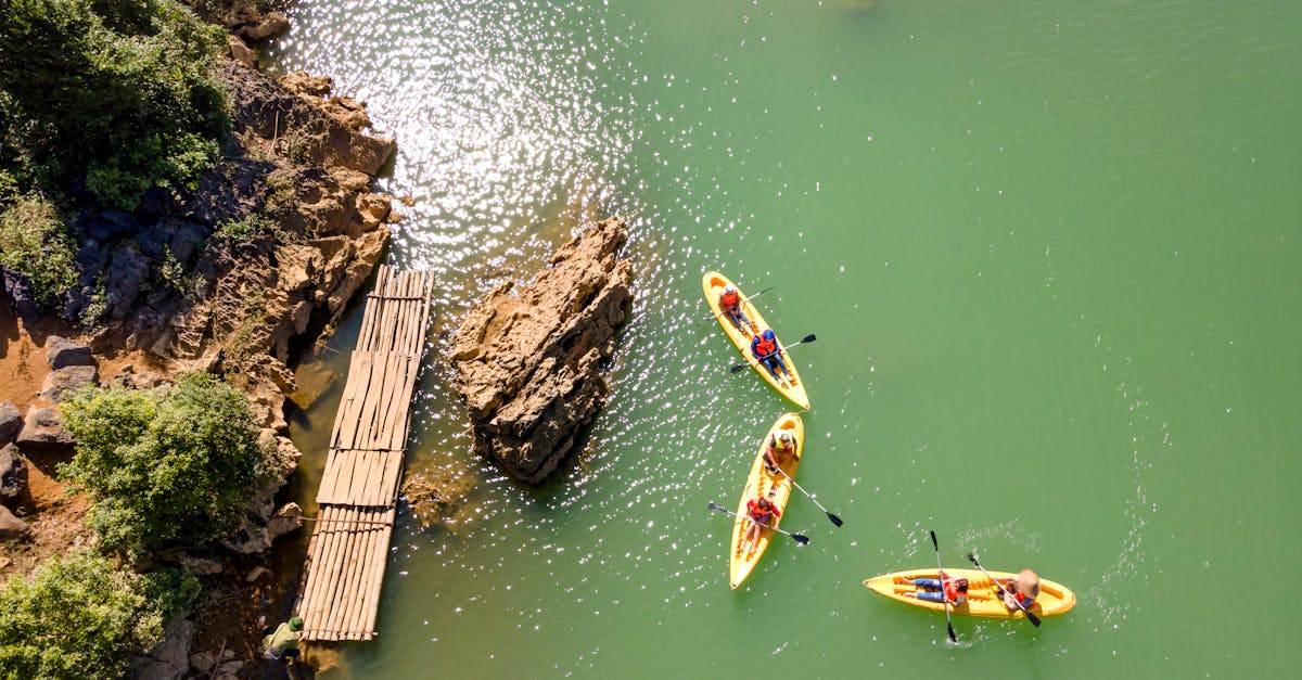 Aerial shot of three kayaks with people paddling near a rocky shore and an old wooden pier.