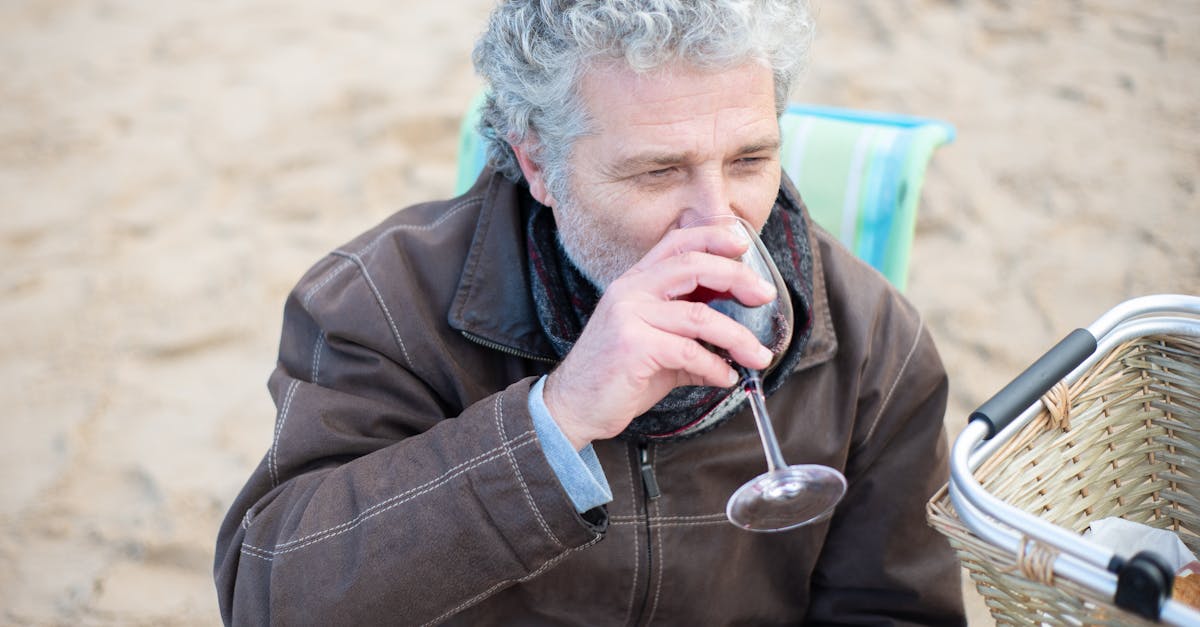 Senior man savoring a glass of red wine on a beach picnic. Relaxed and enjoyable outdoor moment.
