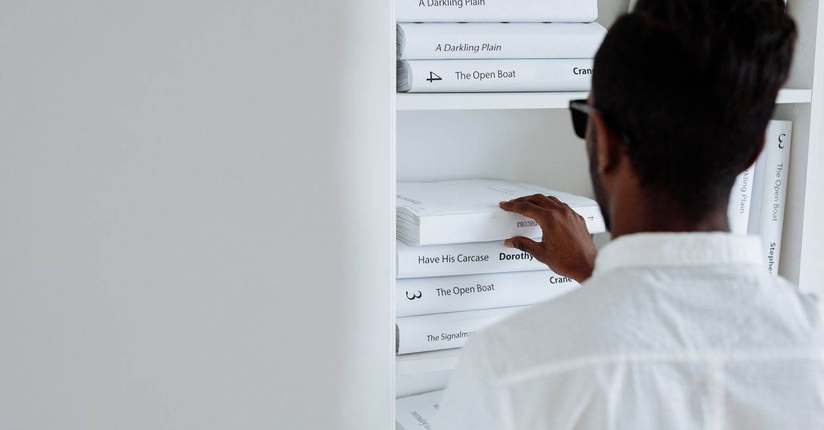 Adult browsing books on a minimalist white shelf, focusing on modern design.