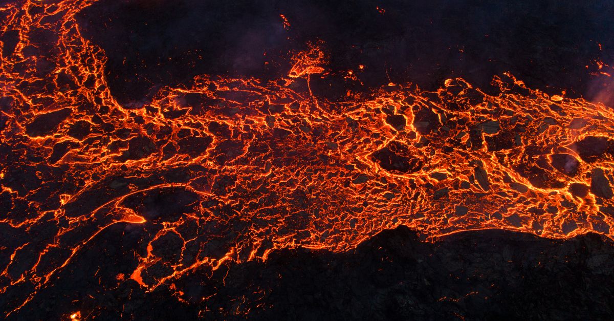 Dramatic aerial view of red-hot lava flowing over dark terrain.