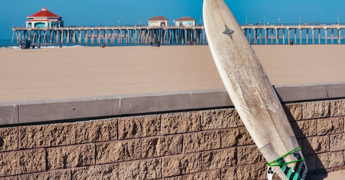 A surfboard rests against a brick wall with a beach pier in the background, perfect for summer vibes.