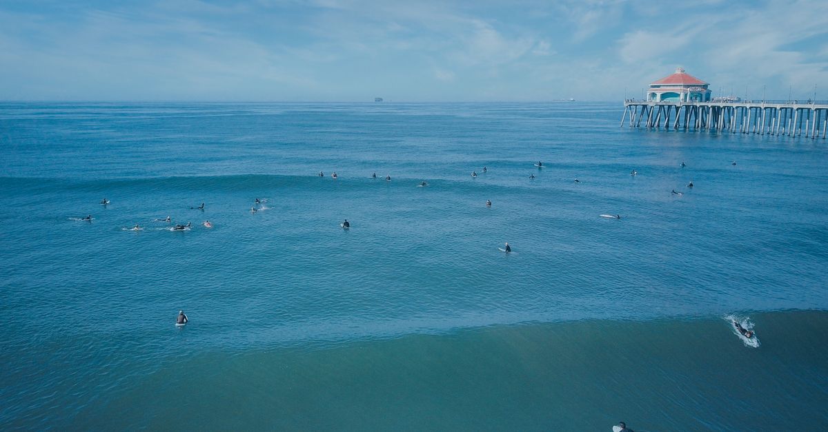 Surfers catching waves near a famous pier on a clear sunny day.