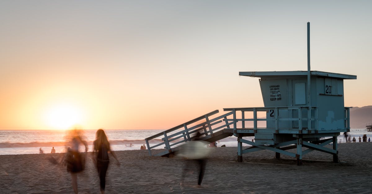 Beach scene at sunset with a lifeguard tower and people in motion at Santa Monica, CA.