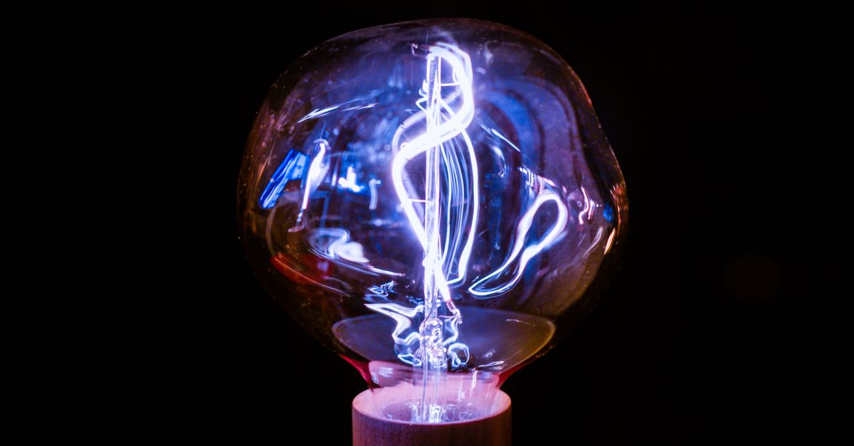 Close-up of a glowing vintage light bulb with an intricate filament design against a dark background.