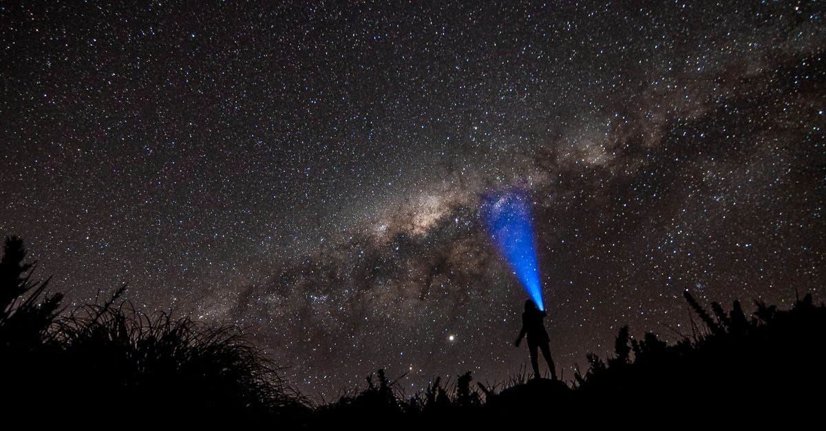 Person with flashlight under the starlit sky of the Milky Way galaxy at night.