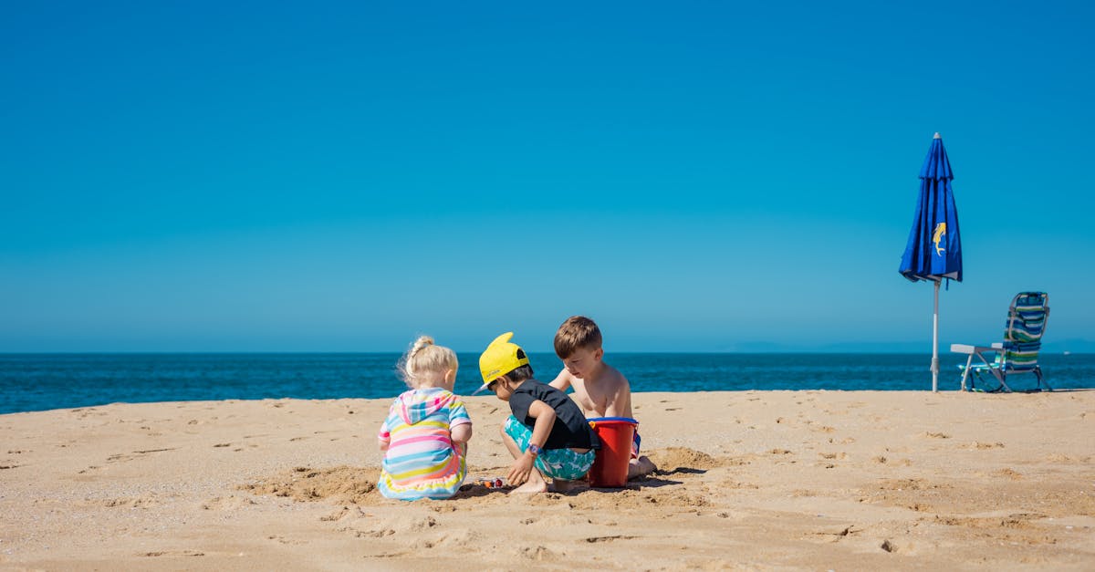 Three children playing on a sunny beach with blue sky, sand, and ocean view. Perfect summer vacation scene.