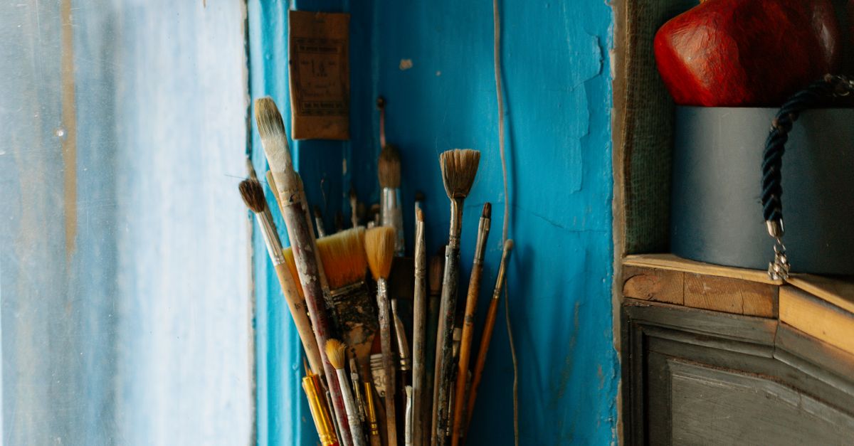 A rustic collection of paintbrushes against a textured blue wall, capturing artistic inspiration.
