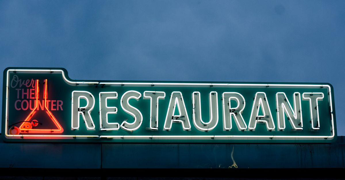 Gleaming neon restaurant sign with vibrant colors against a dusk sky, perfect for urban nightlife themes.