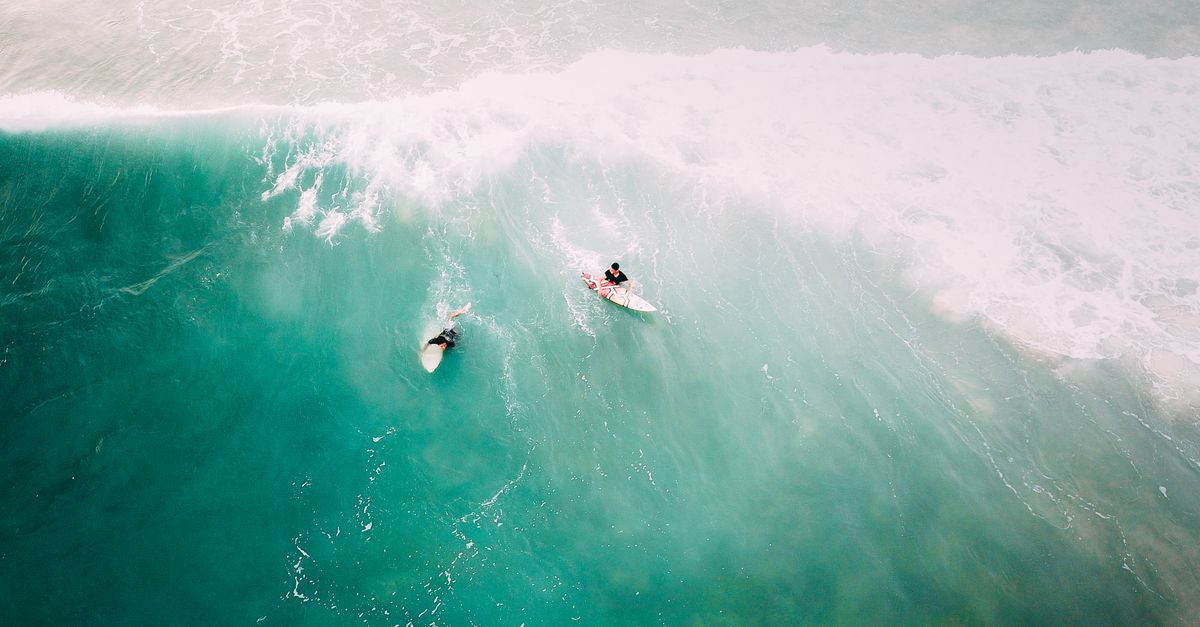 Drone shot of surfers on turquoise waves in Pahang, Malaysia, highlighting water sports adventure.