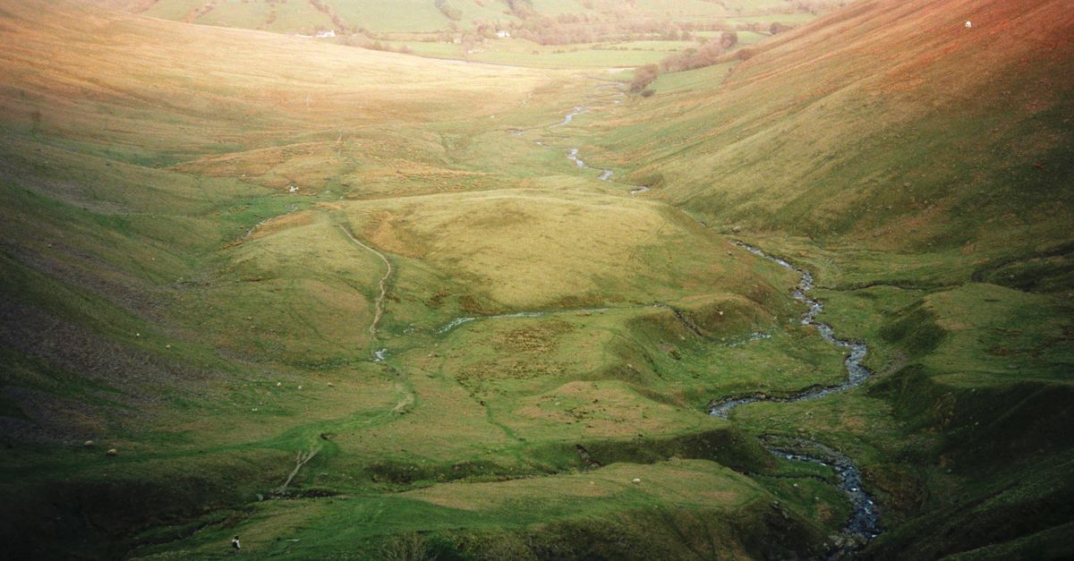 A tranquil view of England's lush countryside featuring a meandering creek and rolling hills.