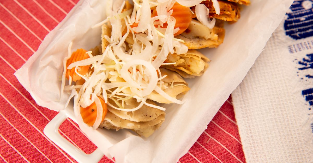 Close-up of authentic Mexican tacos with fresh onions and carrots on a white platter.