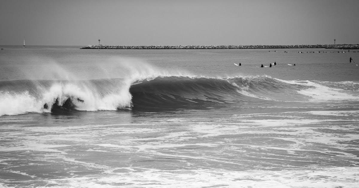 Monochrome seascape capturing ocean waves and surfers near a breakwater.