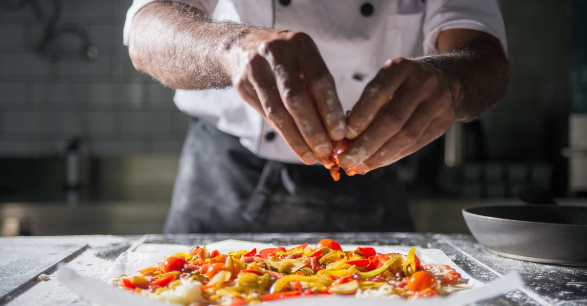 Chef adds final toppings to a colorful dish in a professional kitchen.