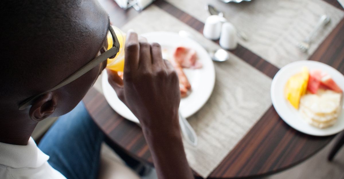 Close-up of a man drinking juice, enjoying a breakfast spread at a stylish table.