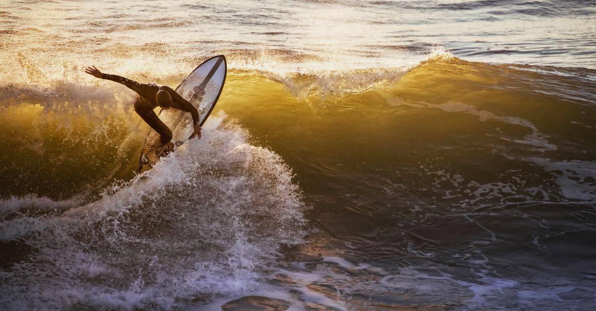 A surfer skillfully rides a wave during a golden sunset at Pismo Beach, California, epitomizing water sport excitement.