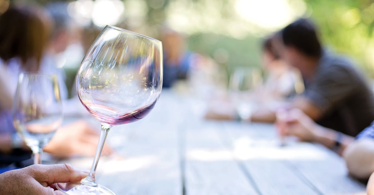 Wine glass with red wine on a wooden table at an outdoor gathering with blurred people.